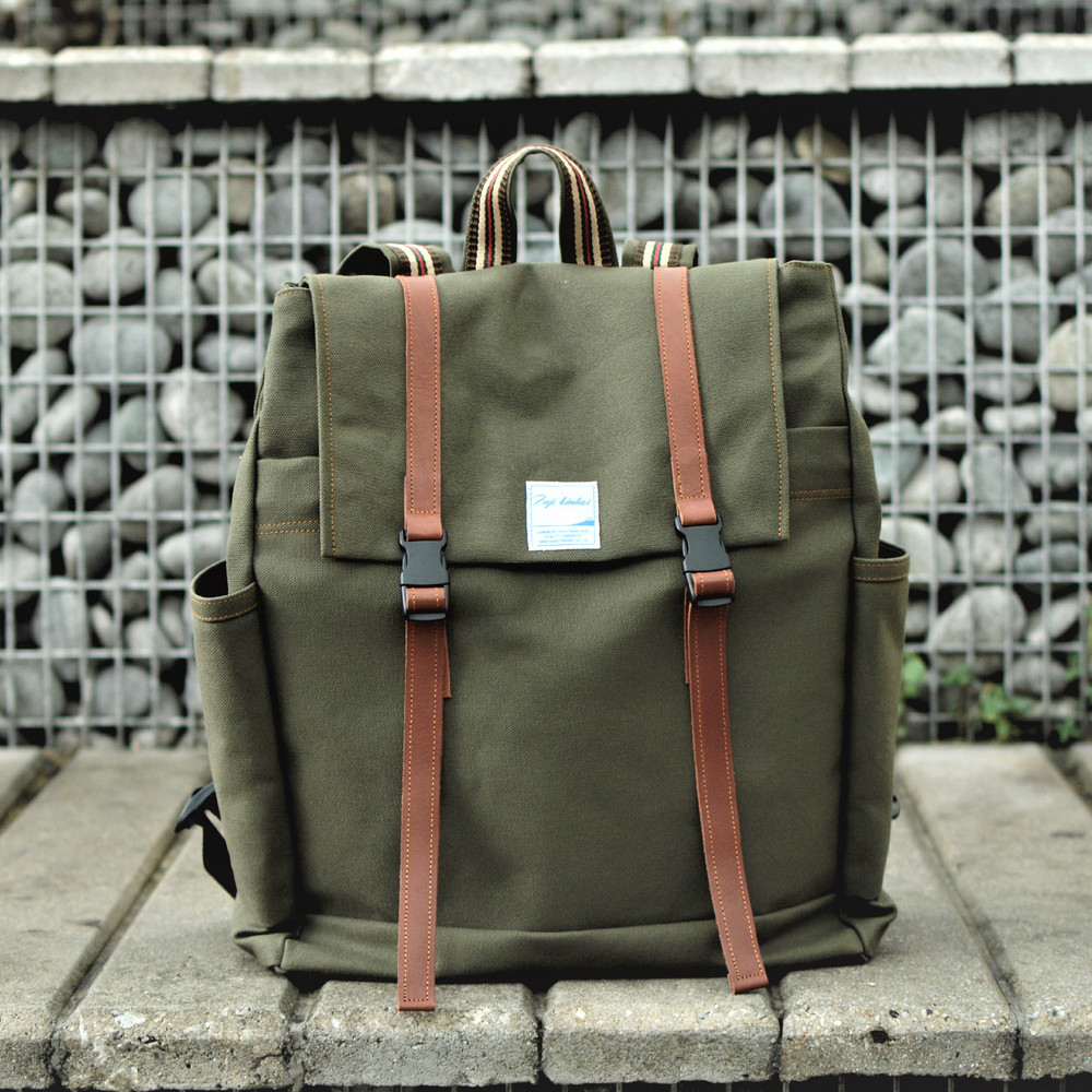 Green backpack with brown straps on a stone surface with a metal grid background