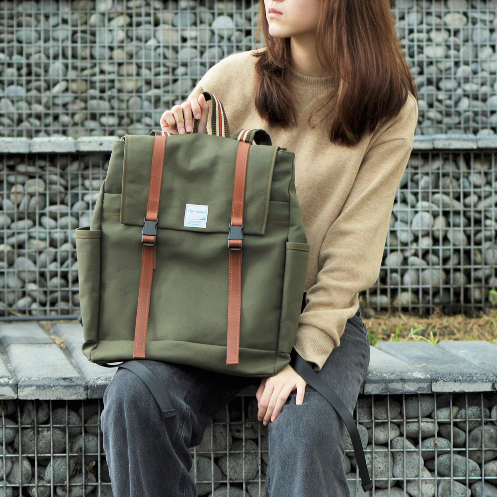 Person holding a green backpack with brown straps against a stone wall background
