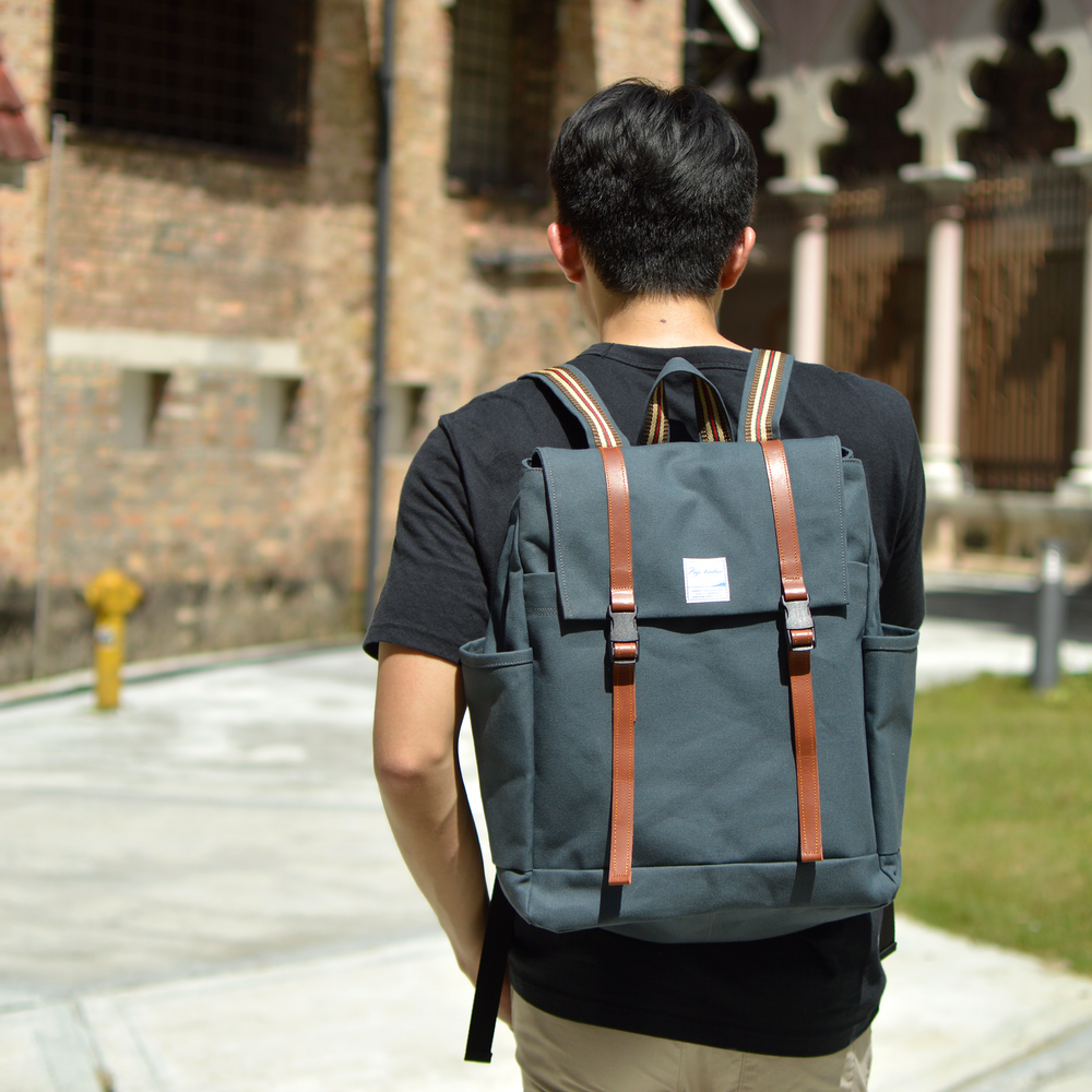 Person wearing a dakr blue backpack with brown straps outdoors.