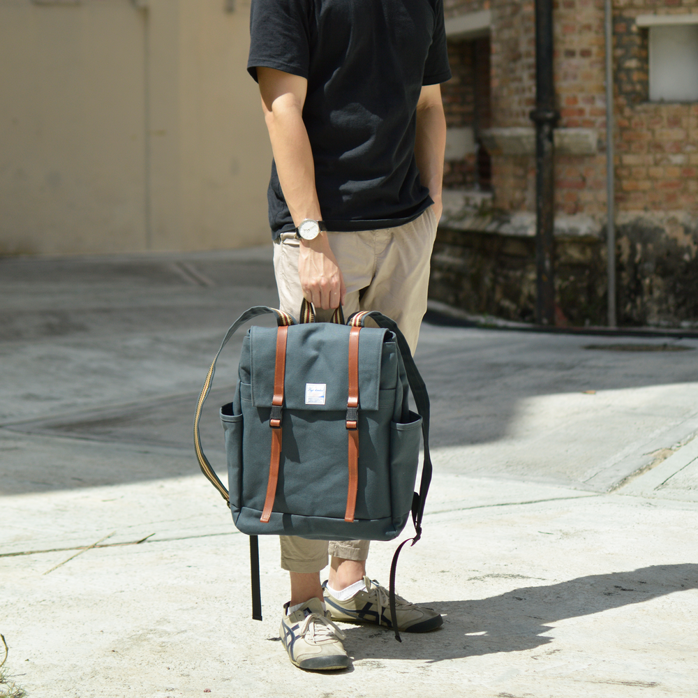 Person holding a blue backpack with brown straps on a street.