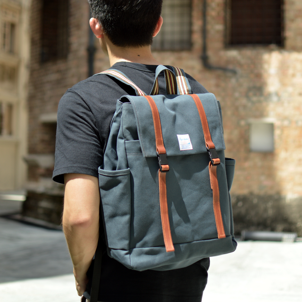 Person wearing a gray backpack with brown leather straps in an urban setting