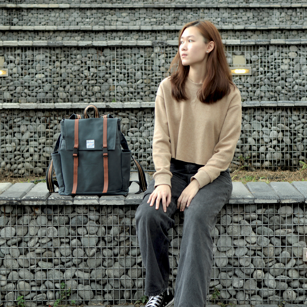 Woman sitting on a stone wall with a dark blue backpack next to her against a textured wall background