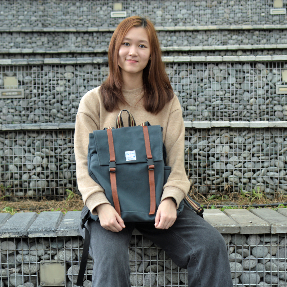 Woman holding a blue backpack with brown straps against a stone wall background