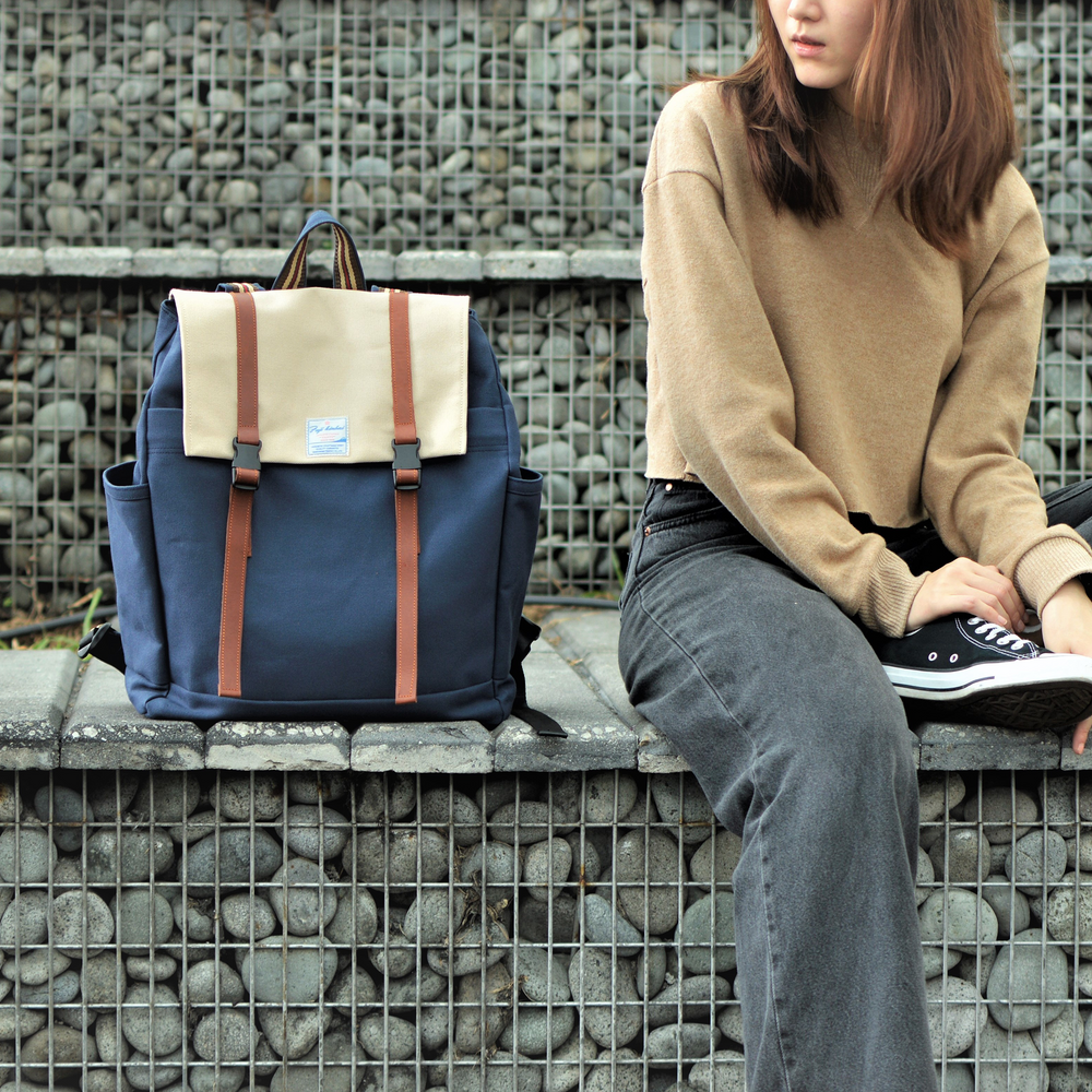 Person sitting on a stone wall with a blue backpack featuring beige accents.