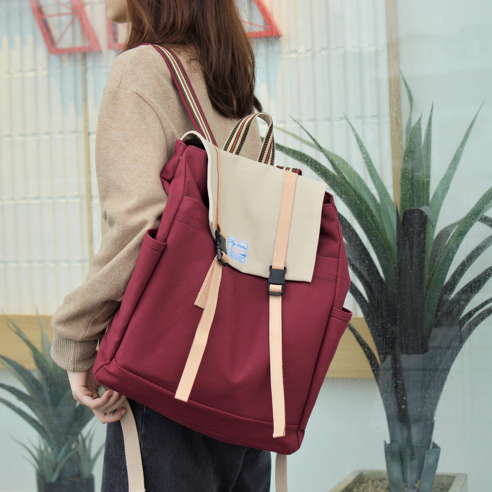 Person holding a red and beige backpack with plants in the background