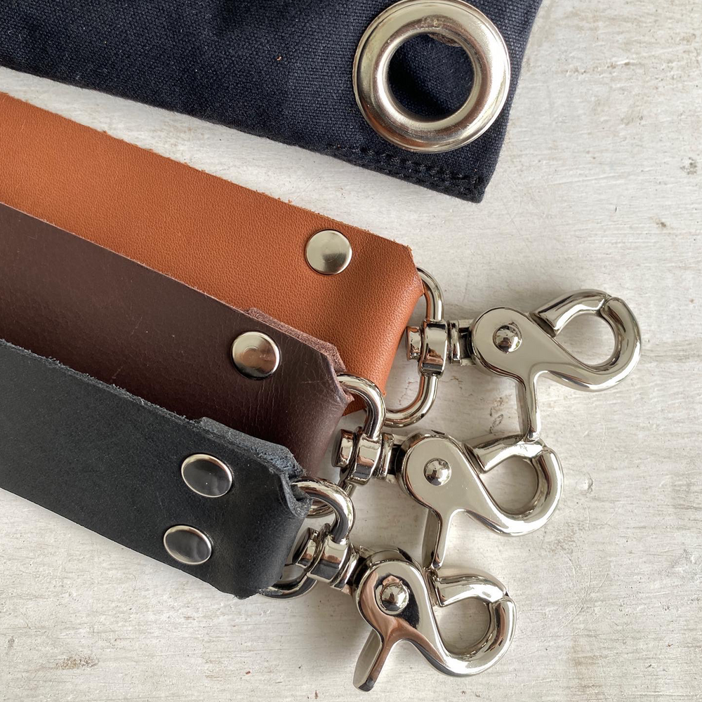 Close-up of leather straps with metal hooks on a light gray surface.