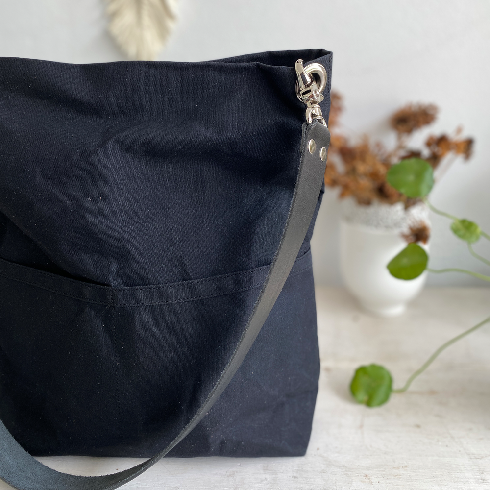 Black bag with a zipper on a light surface with plants in the background