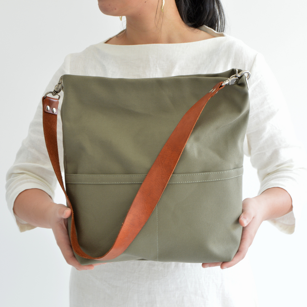 Person holding a green shoulder bag with a brown strap on a white background