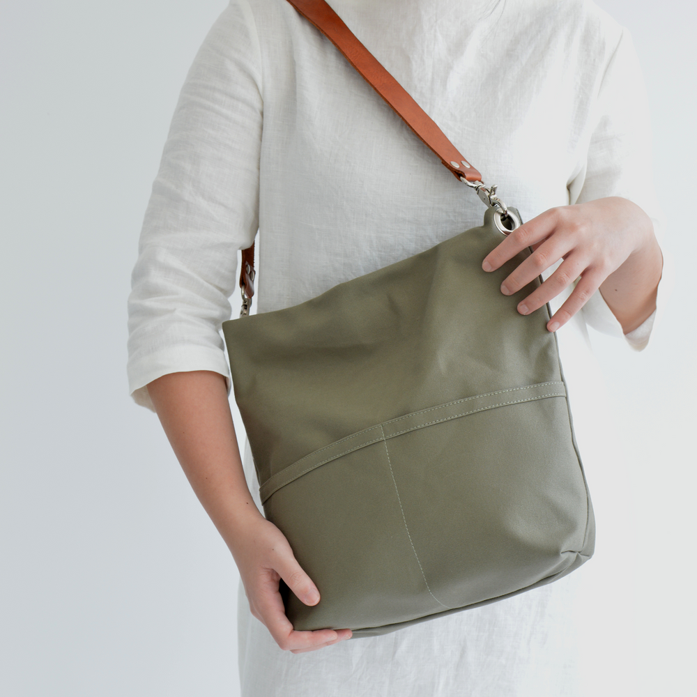 Person holding a green shoulder bag with a plain background