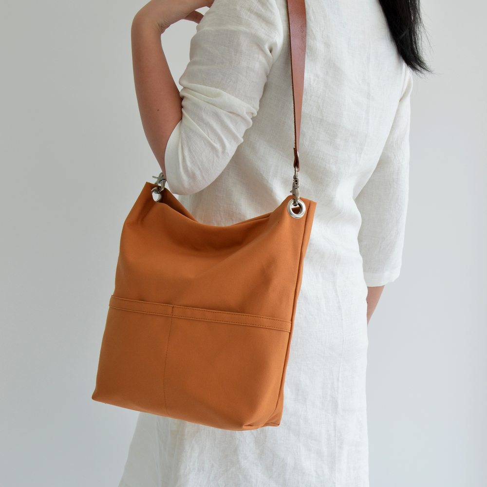 Person wearing a white outfit with an orange shoulder bag on a plain background