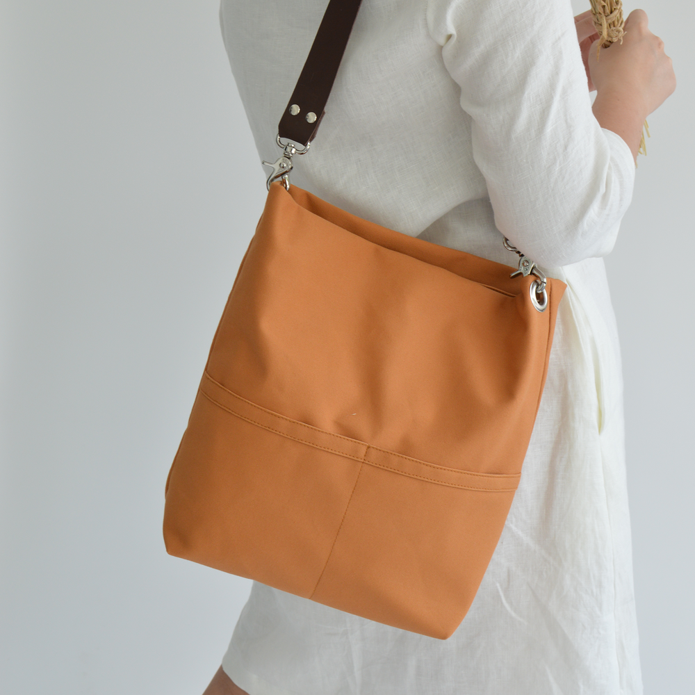 Orange shoulder bag held by a person wearing a white outfit on a plain background