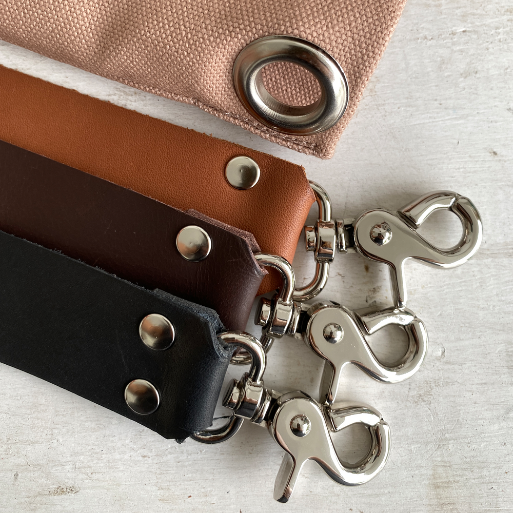 Three different coloured leather bag straps, flat lay on textured background.