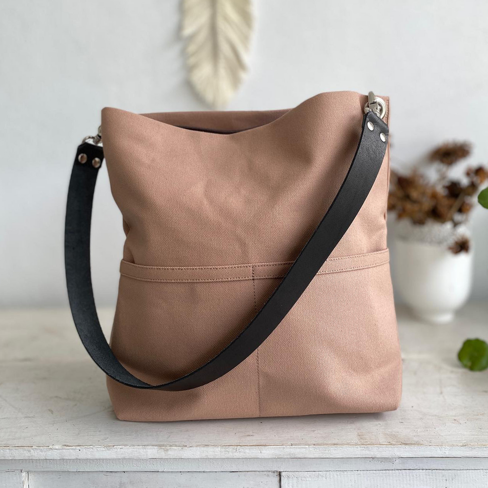 Light brown bag with black leather straps on a desk against plain background.