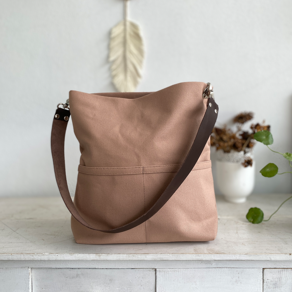 Light brown shoulder bag with brown leather straps against plain background.
