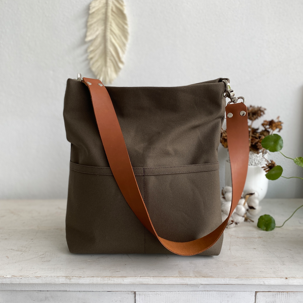 Brown tote bag with light brown strap on a white surface with decorative elements in the background